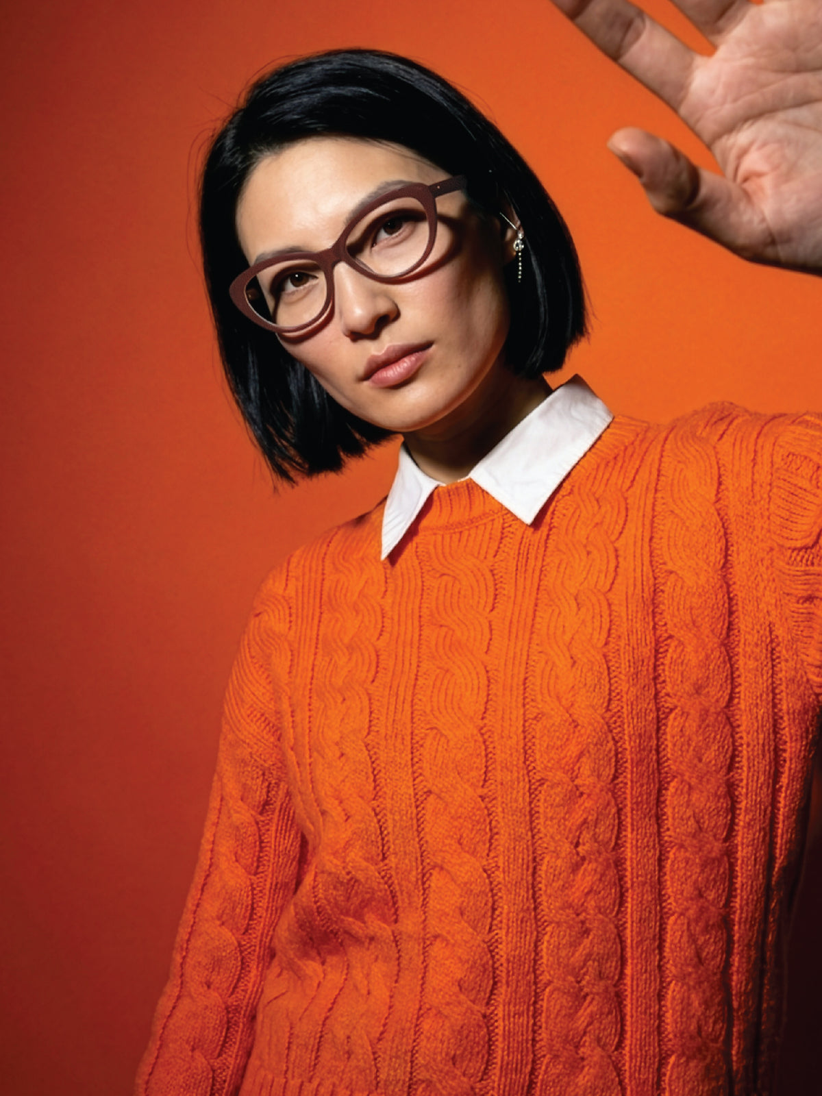 Editorial shot of a model in an orange cable-knit sweater wearing Blynq Ora Cordovan frames