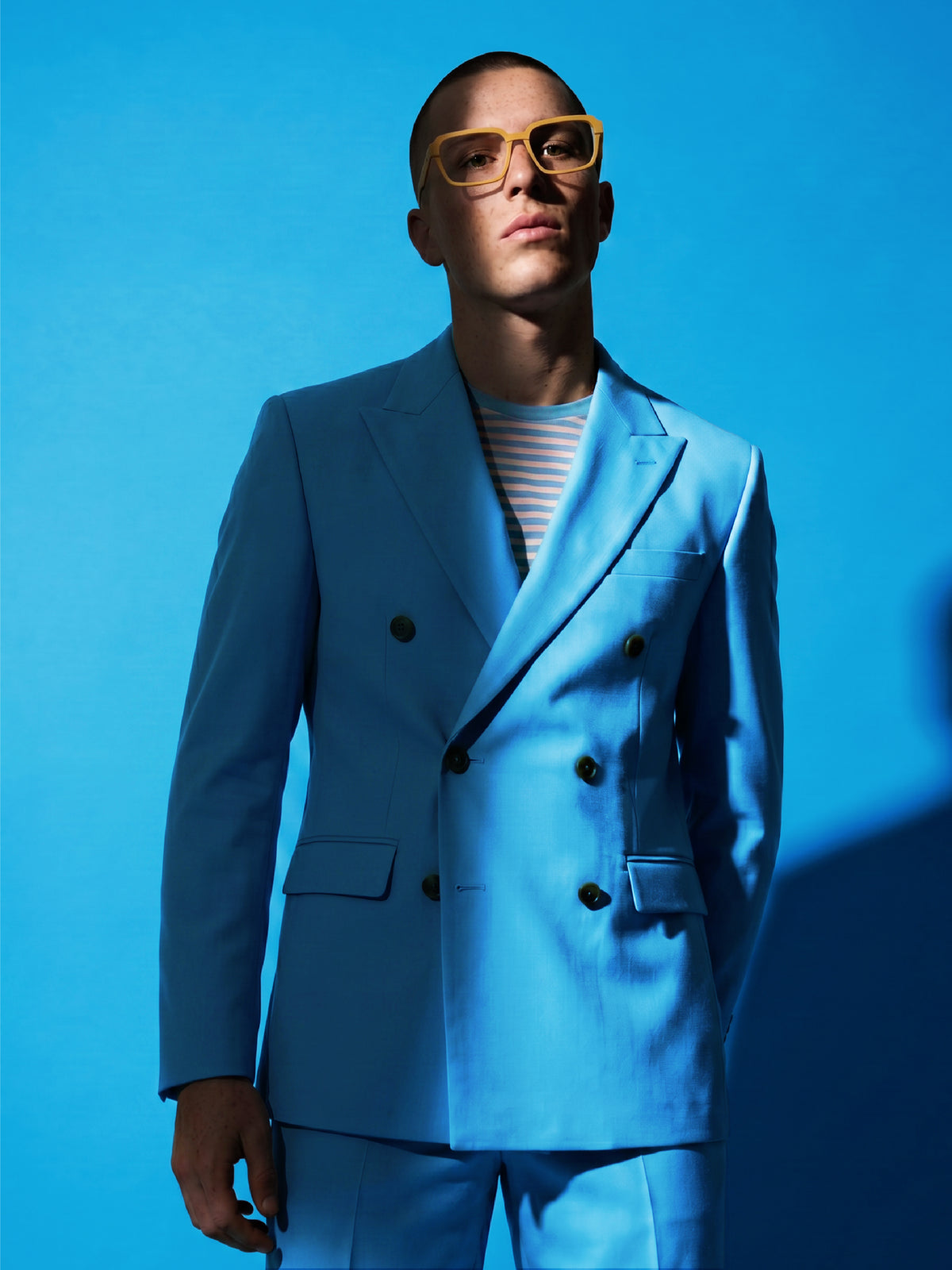 Editorial shot of a model in a bright blue suit wearing Blynq Quad Dune frames