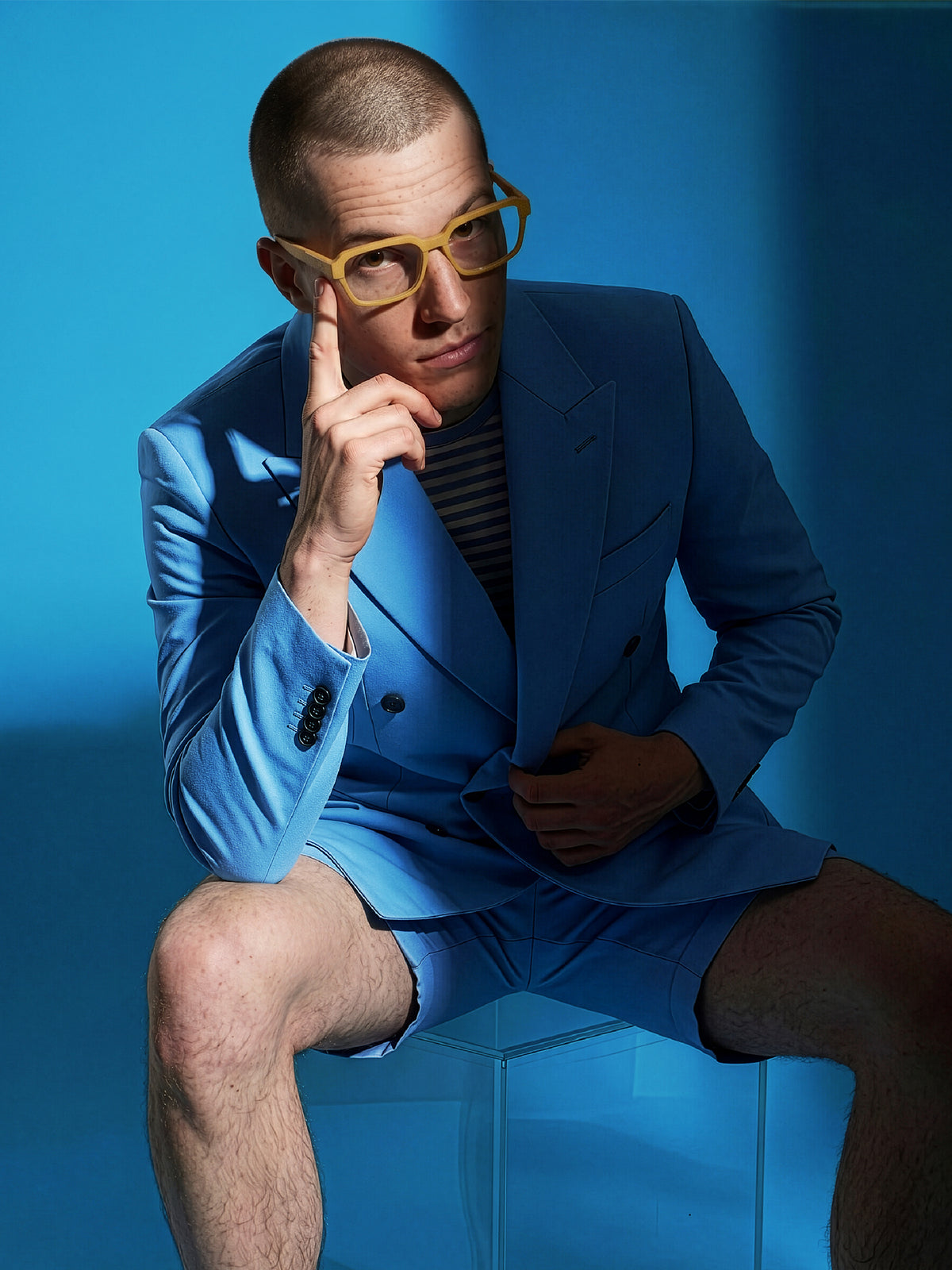 Seated model in a bright blue suit wearing Blynq Quad square glasses in Dune